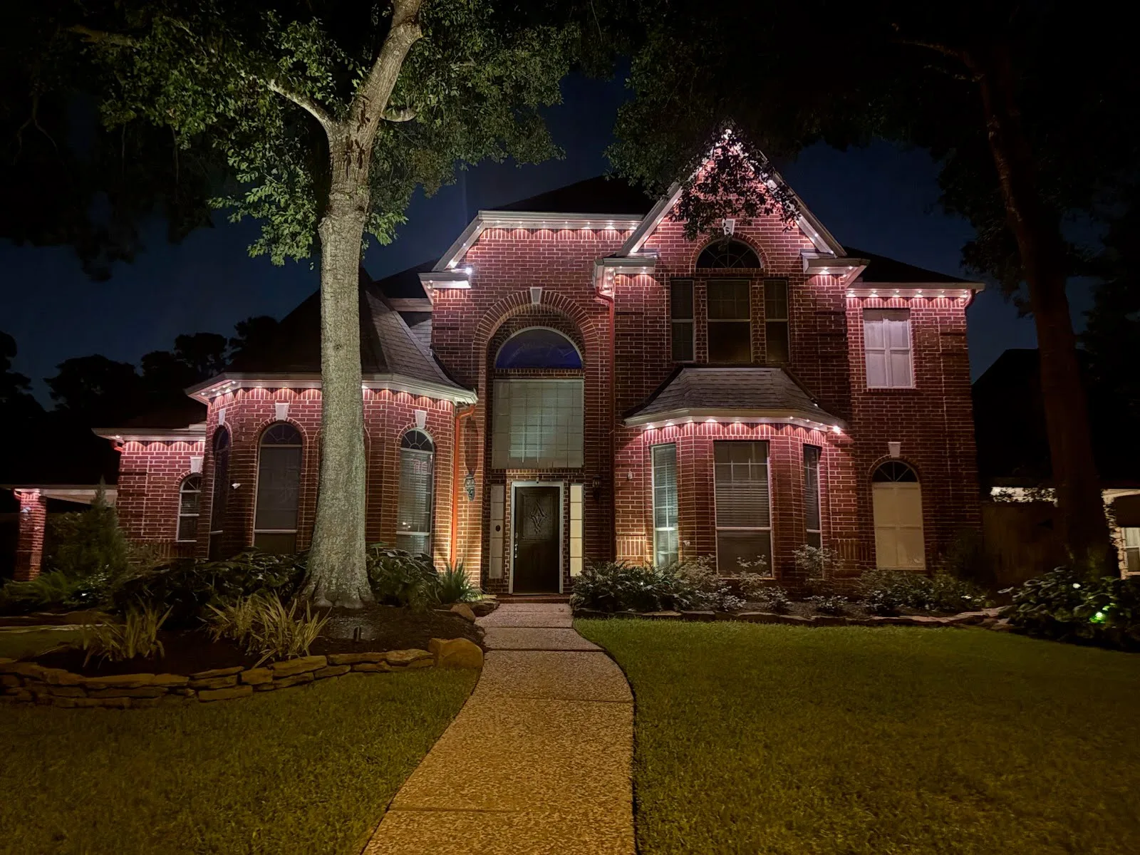 Real Skyclear install — two-story Houston brick home outlined in warm-white permanent roofline lighting at night